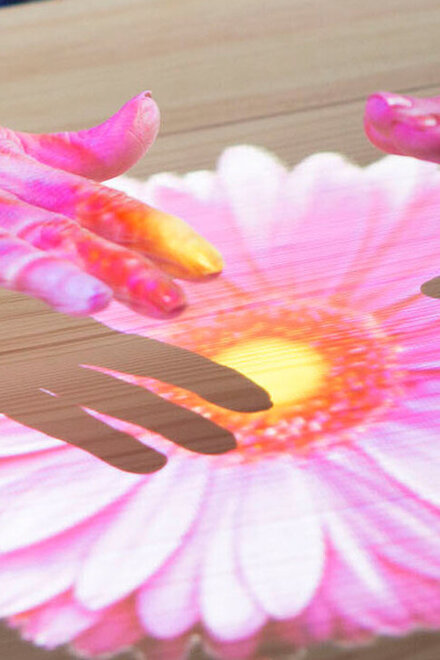 Hände auf einem  Blumenbild, das über die Tovertafel auf einen Tisch projiziert ist.
