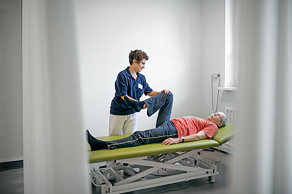 Eine Physiotherapeutin behandelt das Bein eines Senioren in einer Reha-Klinik.